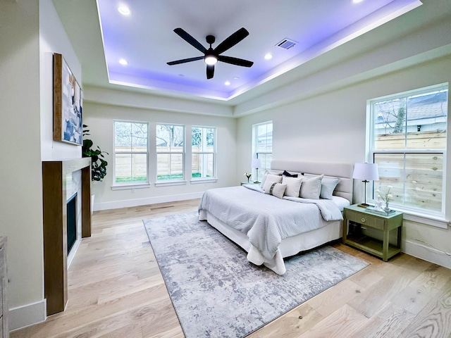 bedroom featuring a fireplace, a raised ceiling, visible vents, light wood-style flooring, and baseboards