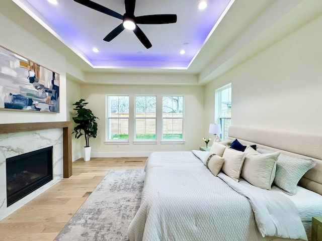 bedroom featuring recessed lighting, a raised ceiling, light wood-style floors, a high end fireplace, and baseboards