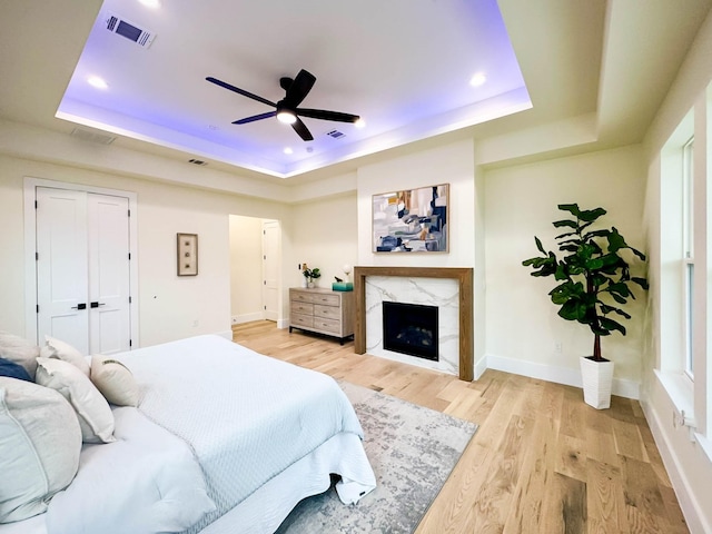 bedroom with a tray ceiling, visible vents, a fireplace, and light wood-style flooring