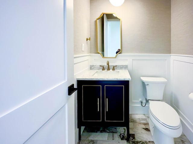 half bath with toilet, a wainscoted wall, a decorative wall, and vanity