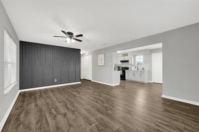 unfurnished living room with a ceiling fan, dark wood-style flooring, a sink, and baseboards