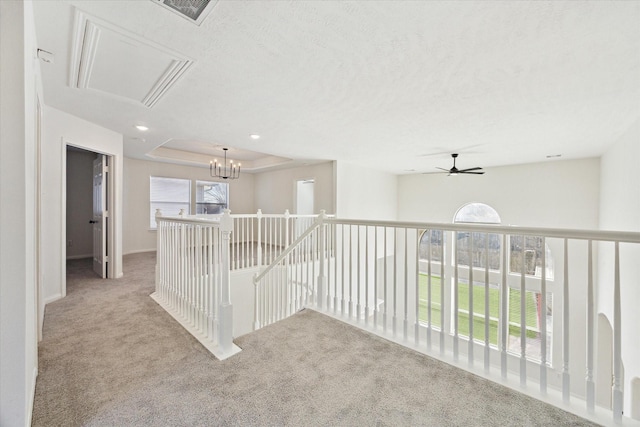 hall with a textured ceiling, a chandelier, light carpet, an upstairs landing, and a raised ceiling