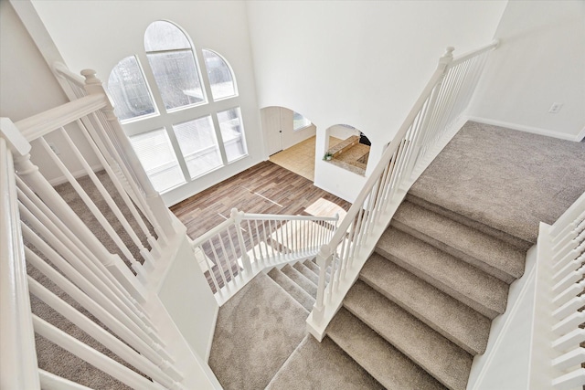 stairway with plenty of natural light, a high ceiling, arched walkways, and wood finished floors