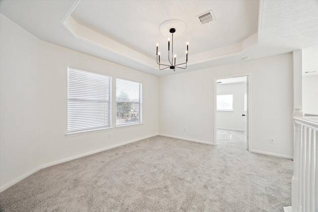 spare room featuring a tray ceiling, a healthy amount of sunlight, visible vents, and a notable chandelier