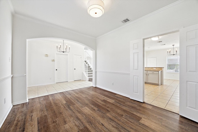 foyer entrance featuring a chandelier, arched walkways, light wood-type flooring, and ornamental molding