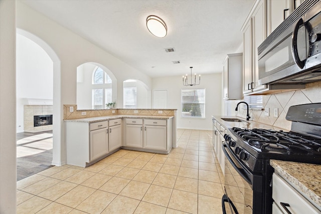 kitchen with light tile patterned floors, black appliances, tasteful backsplash, and decorative light fixtures