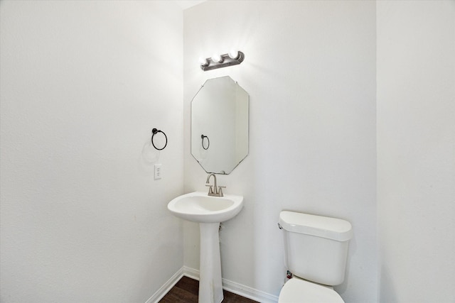 half bathroom with wood finished floors, toilet, and baseboards