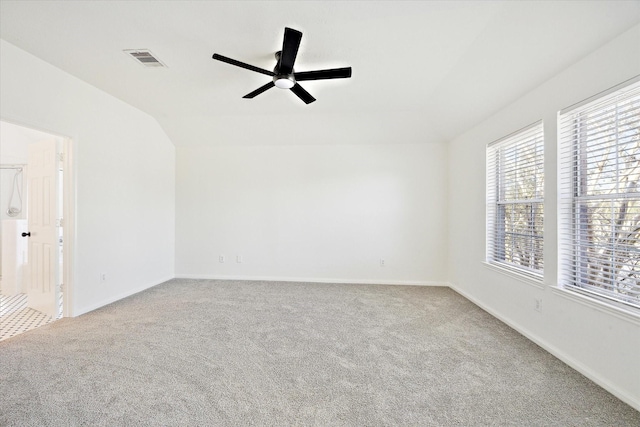 carpeted empty room with baseboards, visible vents, vaulted ceiling, and a ceiling fan