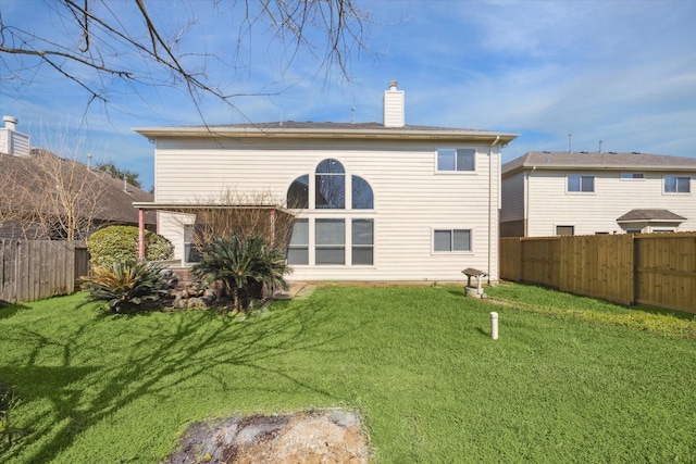 back of property with a fenced backyard, a yard, and a chimney