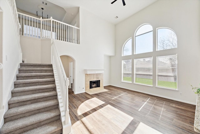 unfurnished living room with a ceiling fan, baseboards, a tiled fireplace, and wood finished floors