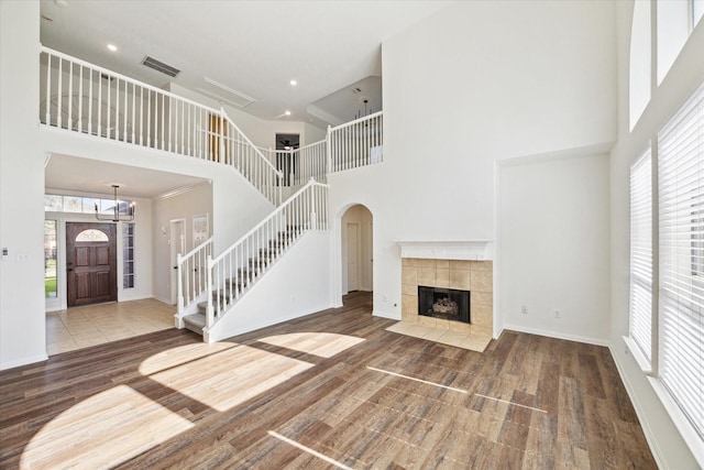 unfurnished living room with visible vents, a towering ceiling, wood finished floors, stairs, and a fireplace