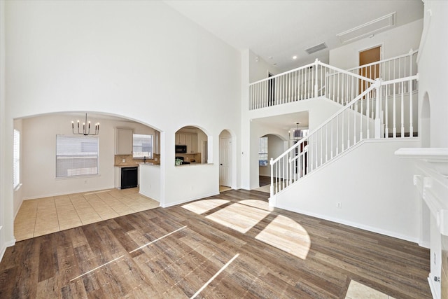 unfurnished living room with light wood-style floors, visible vents, an inviting chandelier, and stairs