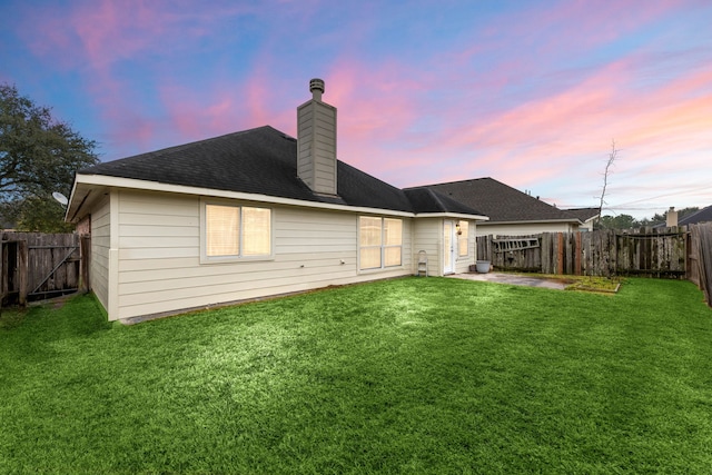 back of house at dusk with a shingled roof, a lawn, a chimney, and a fenced backyard