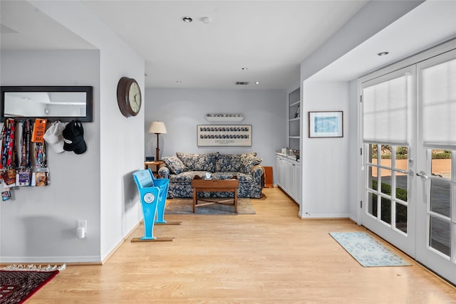 living room with visible vents, built in features, baseboards, light wood-style flooring, and french doors