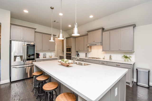 kitchen featuring stainless steel appliances, gray cabinetry, a sink, under cabinet range hood, and a kitchen bar