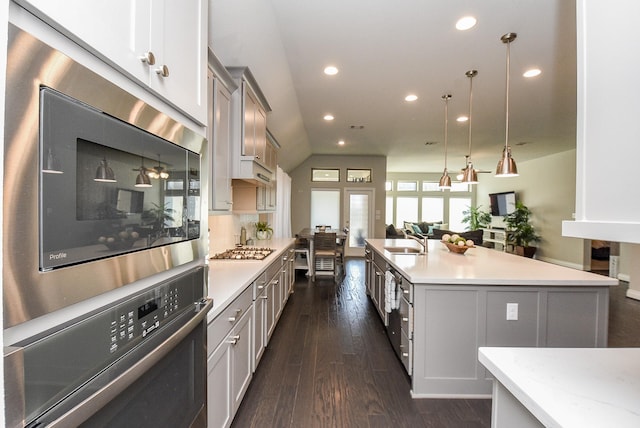 kitchen with dark wood finished floors, stainless steel appliances, light countertops, open floor plan, and a sink