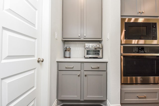 kitchen with decorative backsplash, oven, built in microwave, light countertops, and gray cabinetry