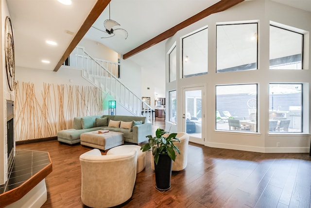 living room with dark wood finished floors, stairway, beamed ceiling, a fireplace, and high vaulted ceiling