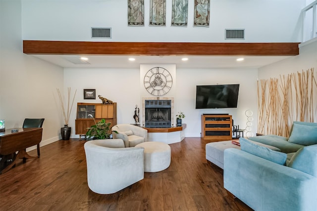 living room featuring dark wood-style floors, beam ceiling, visible vents, and a tiled fireplace