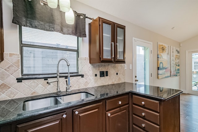 kitchen featuring a peninsula, a sink, dark brown cabinets, dark stone counters, and glass insert cabinets