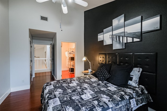 bedroom featuring dark wood-style flooring, visible vents, a high ceiling, ensuite bathroom, and baseboards