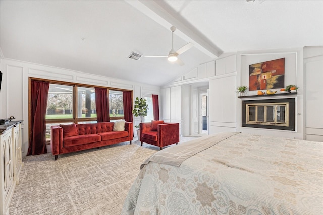 bedroom featuring lofted ceiling with beams, a decorative wall, light carpet, visible vents, and a glass covered fireplace