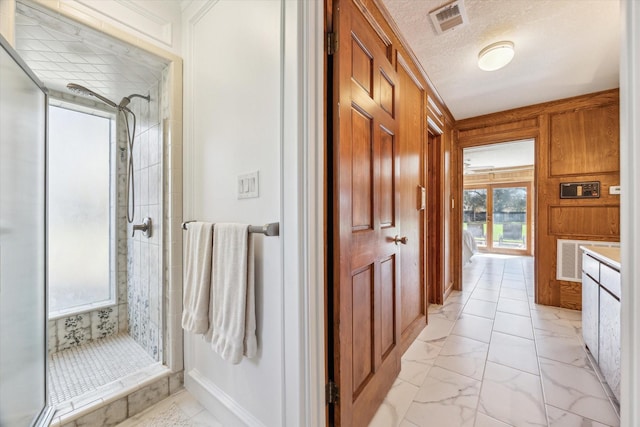 bathroom with a textured ceiling, wooden walls, visible vents, marble finish floor, and a shower stall