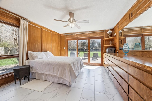 bedroom with marble finish floor, ceiling fan, wooden walls, a textured ceiling, and access to outside