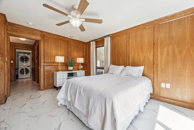 bedroom featuring marble finish floor, wooden walls, a ceiling fan, and stacked washer / drying machine