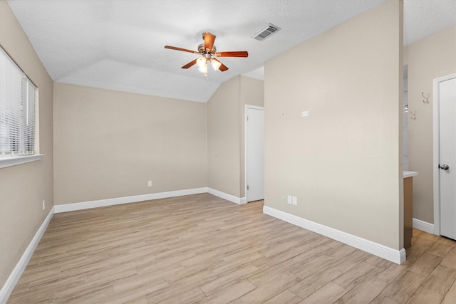 spare room with light wood finished floors, baseboards, visible vents, a ceiling fan, and vaulted ceiling