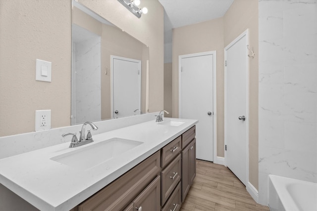 bathroom with double vanity, wood tiled floor, a washtub, and a sink