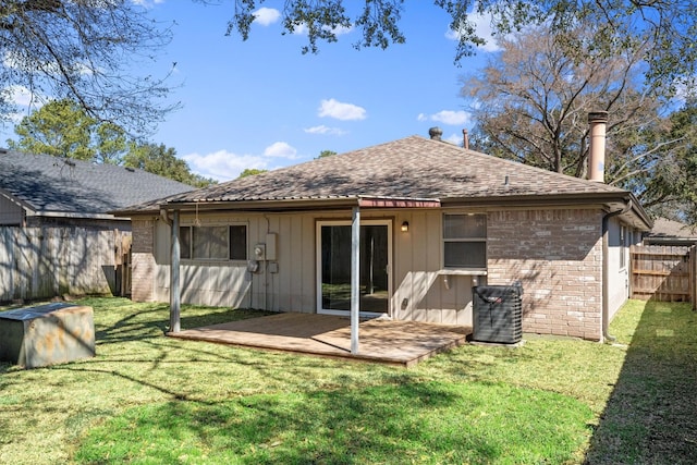 rear view of property featuring cooling unit, brick siding, fence, roof with shingles, and a lawn