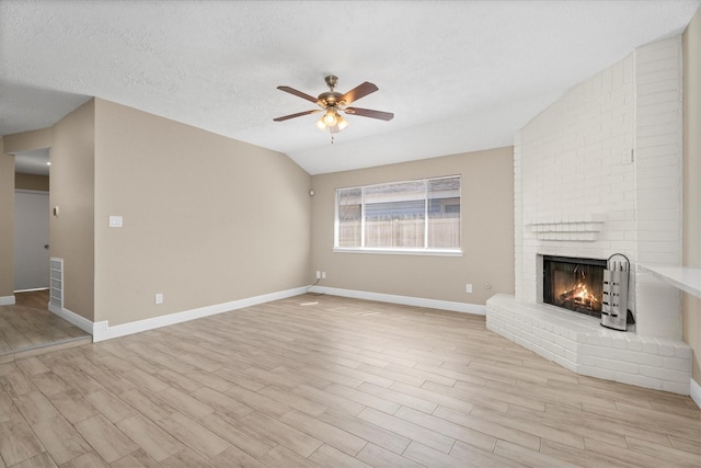 unfurnished living room featuring a textured ceiling, a fireplace, a ceiling fan, vaulted ceiling, and light wood-type flooring