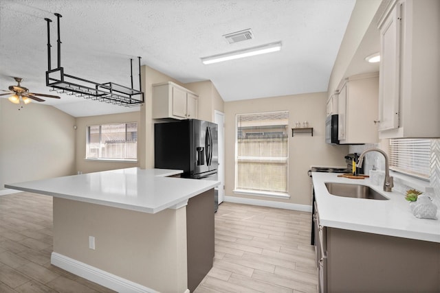 kitchen with refrigerator with ice dispenser, visible vents, light countertops, black microwave, and a sink