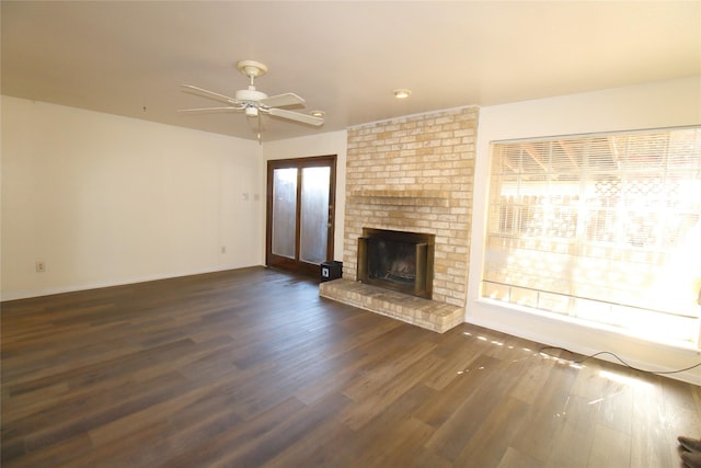 unfurnished living room with dark wood-type flooring, a brick fireplace, a healthy amount of sunlight, and a ceiling fan