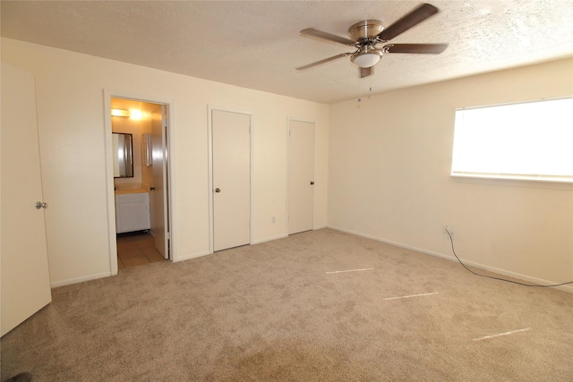 unfurnished bedroom featuring a textured ceiling, connected bathroom, two closets, and light colored carpet