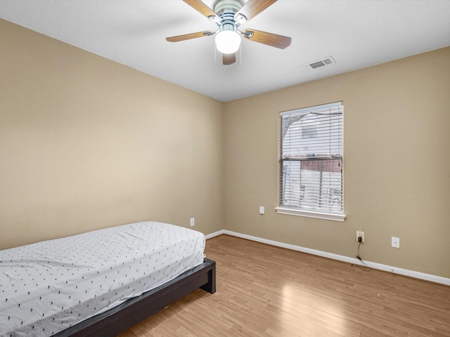 bedroom with light wood-style flooring, a ceiling fan, visible vents, and baseboards