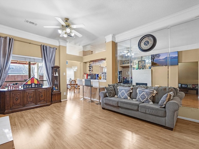 living room with ornamental molding, visible vents, ceiling fan, and light wood finished floors