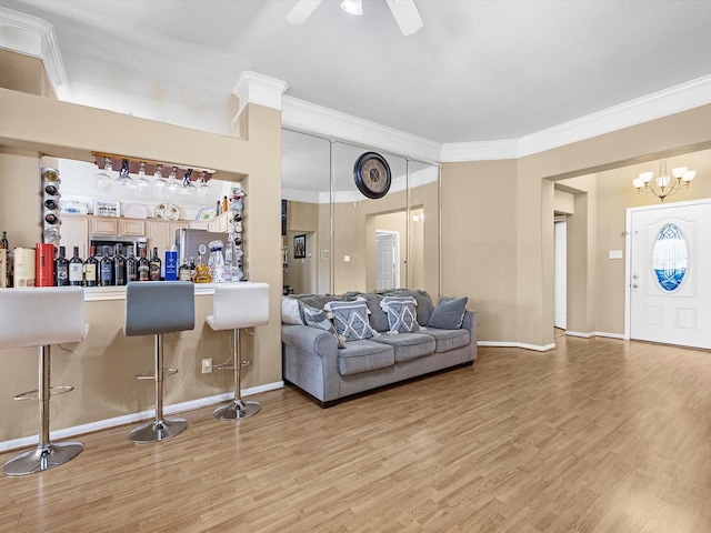 living area featuring crown molding, a dry bar, light wood-style floors, baseboards, and ceiling fan with notable chandelier