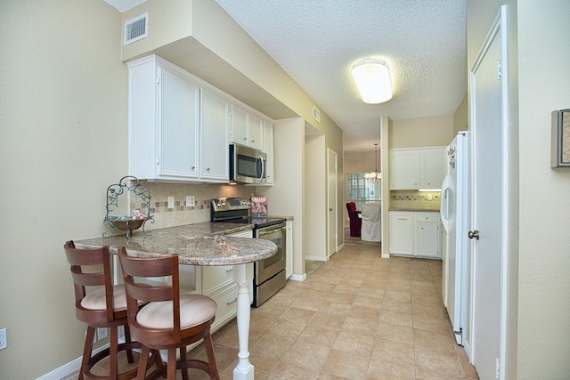 kitchen featuring visible vents, decorative backsplash, appliances with stainless steel finishes, white cabinets, and a peninsula