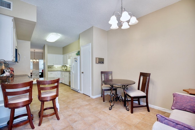 kitchen featuring visible vents, white cabinets, light countertops, white fridge with ice dispenser, and a chandelier