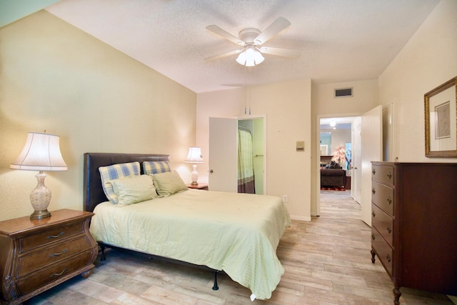 bedroom featuring a textured ceiling, light wood-style flooring, visible vents, baseboards, and a ceiling fan