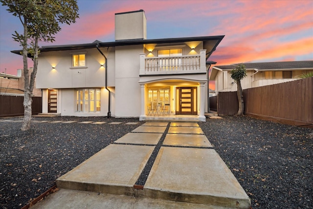 rear view of house with a balcony, fence, stucco siding, a chimney, and a patio area