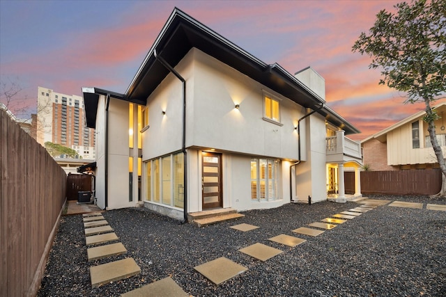 rear view of house featuring a fenced backyard, central AC unit, a balcony, and stucco siding