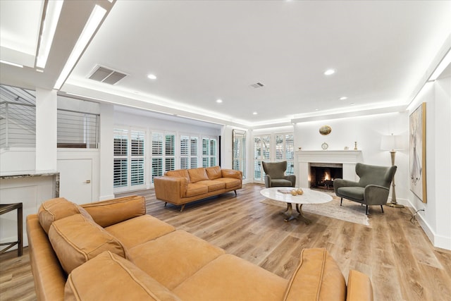 living room with a lit fireplace, recessed lighting, visible vents, and light wood-style floors