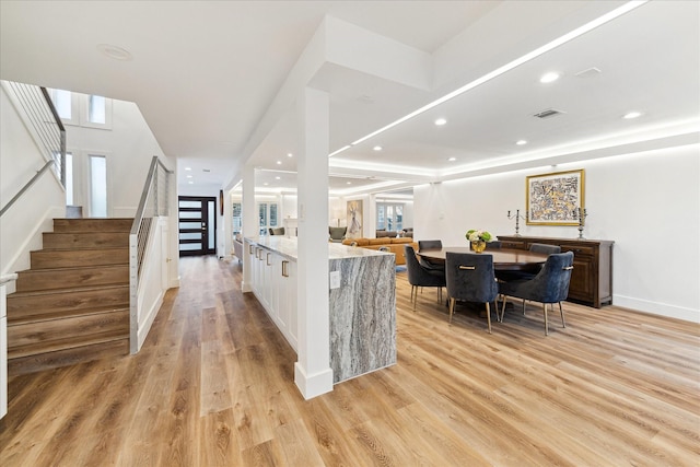 kitchen with light wood-style flooring, white cabinetry, visible vents, and light stone counters