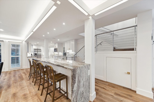 kitchen with light stone counters, stainless steel refrigerator with ice dispenser, light wood-style floors, white cabinets, and a kitchen breakfast bar