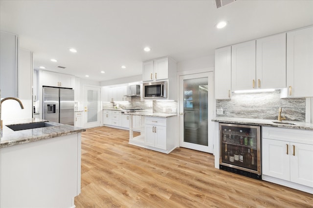 kitchen featuring light stone counters, wine cooler, stainless steel appliances, white cabinets, and a sink