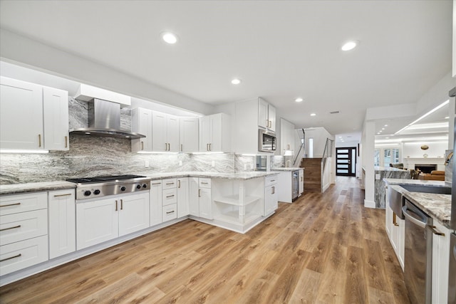 kitchen featuring stainless steel appliances, open floor plan, white cabinets, and wall chimney exhaust hood