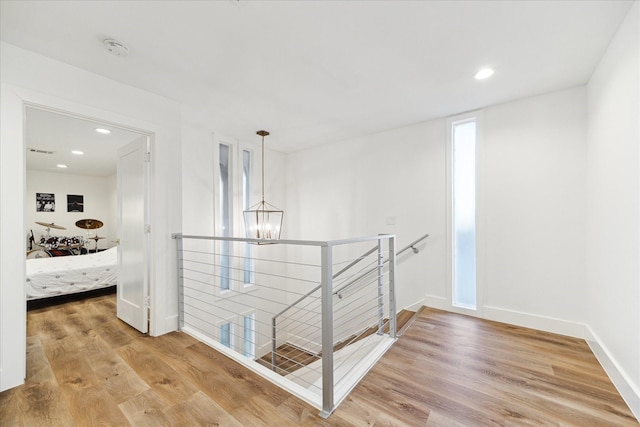 hall featuring light wood-type flooring, baseboards, a notable chandelier, and an upstairs landing